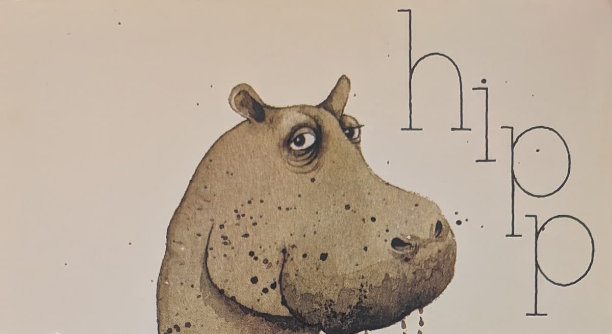 The head of a muddy, dripping hippopotamus. It is looking calmly at the camera